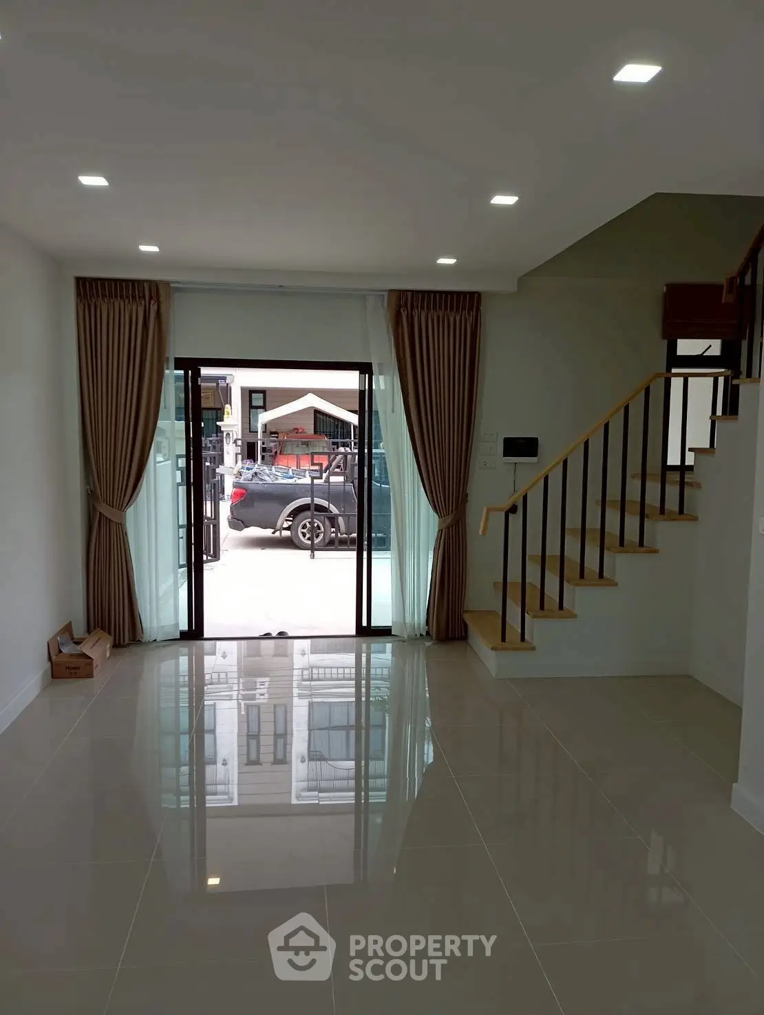 Modern living room with glossy tile flooring and staircase, featuring large glass doors leading to a patio.