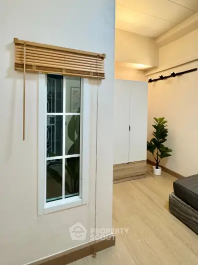 Modern bedroom with minimalist decor, featuring a small window, wooden blinds, and a potted plant for a cozy ambiance.
