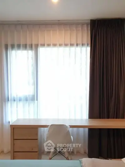 Bright study area with desk and chair by large window with curtains.