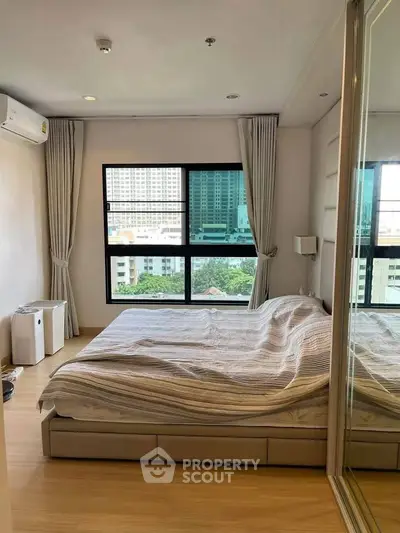 Modern bedroom with large window and city view, featuring sleek mirrored closet doors.