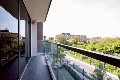 Spacious balcony with glass railing offering a scenic view of lush greenery and modern architecture.