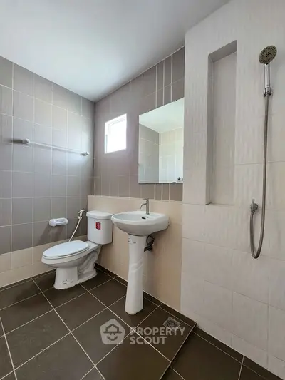 Modern bathroom with sleek design and neutral tiles, featuring a shower and pedestal sink.