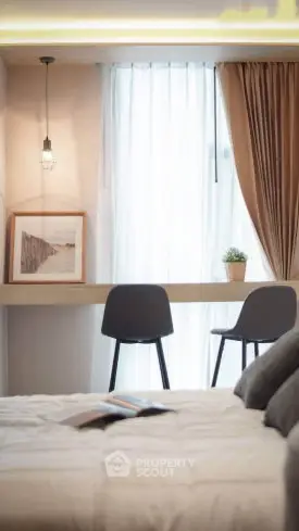 Cozy bedroom with stylish decor and natural light, featuring a modern desk and chairs by the window.