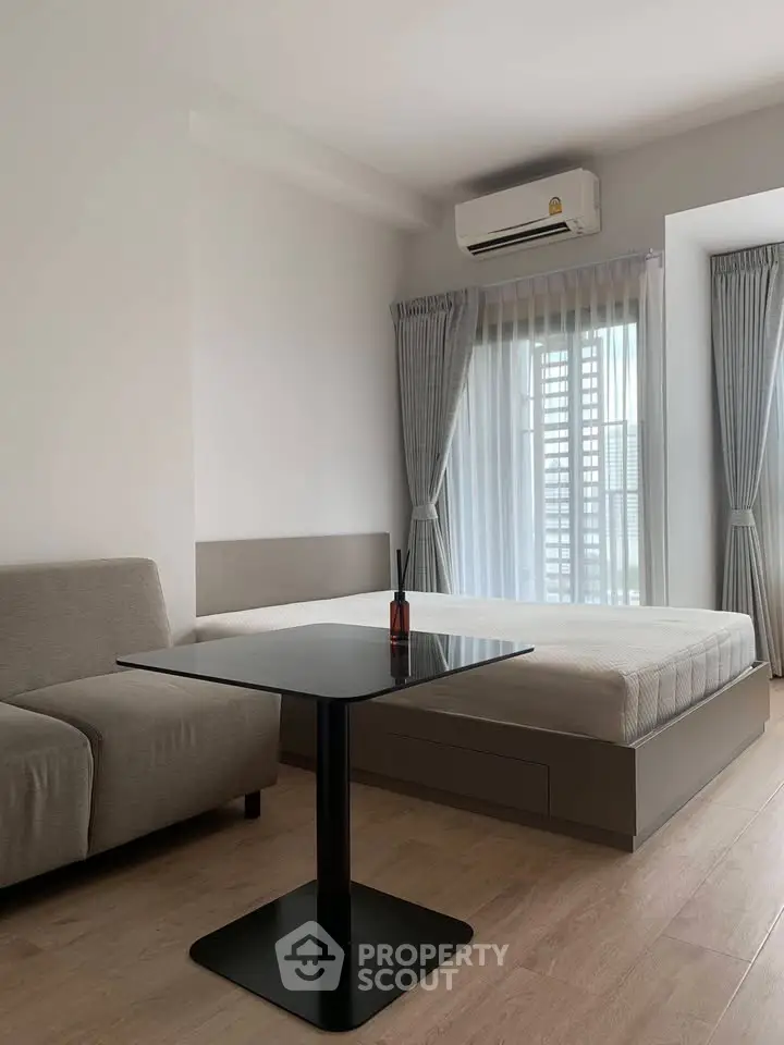 Modern studio apartment with minimalist decor, featuring a cozy bed, sleek table, and air conditioning.