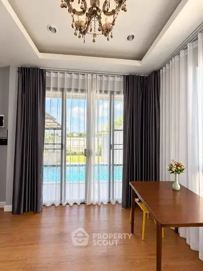 Elegant living room with pool view, chandelier, and stylish curtains, perfect for modern living.