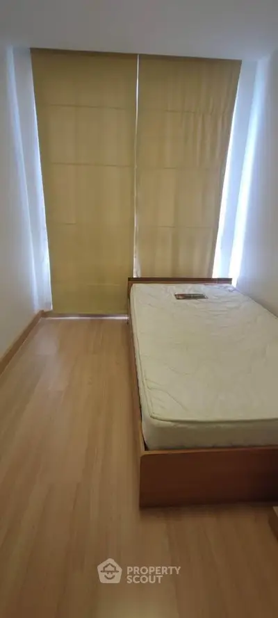 Cozy bedroom with wooden flooring and large window with blinds, featuring a single bed.