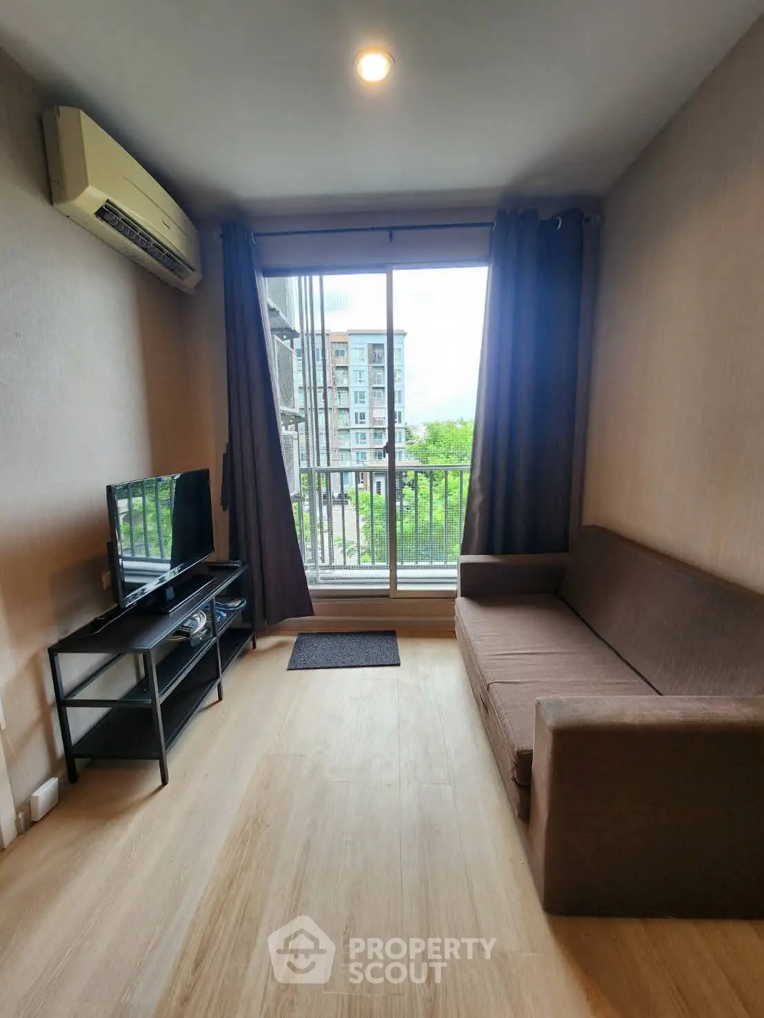 Cozy living room with balcony view, featuring a sofa and TV setup, perfect for relaxation.