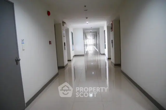 Spacious and well-lit corridor in modern residential building with sleek tile flooring.