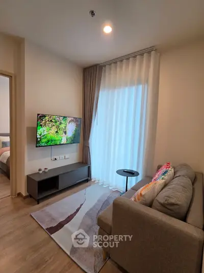 Modern living room with cozy sofa, wall-mounted TV, and large window with sheer curtains.