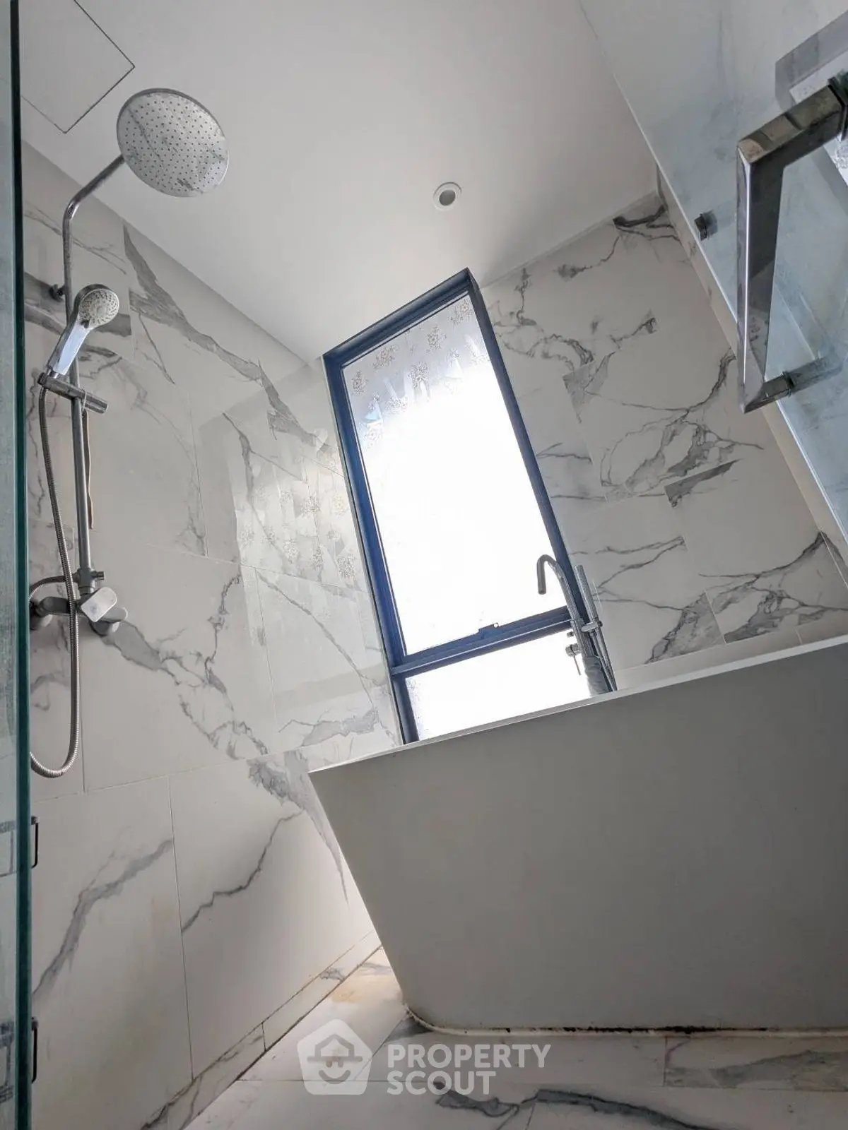Luxurious marble bathroom with modern shower and bathtub, featuring a large window for natural light.