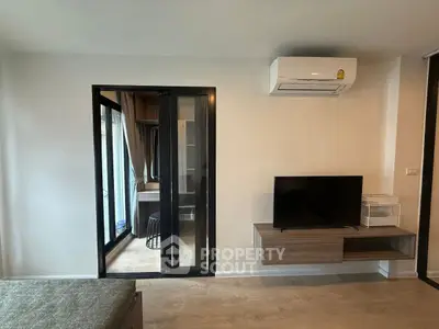Modern living room with air conditioning and sleek TV setup, featuring a glass door leading to a cozy balcony.