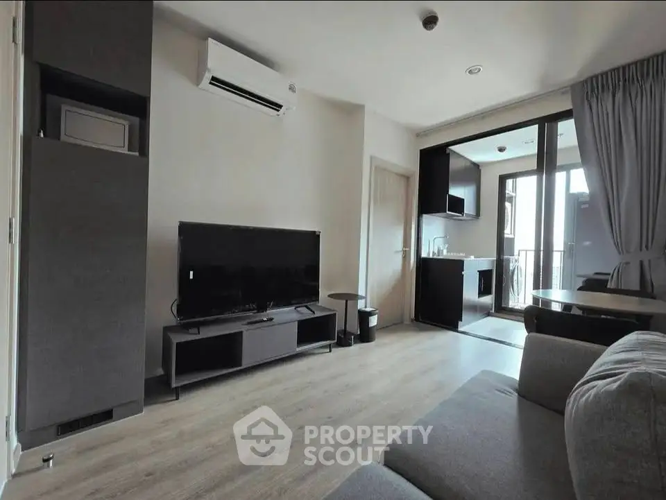 Modern living room with sleek furniture and open kitchen layout, featuring a large TV and air conditioning.