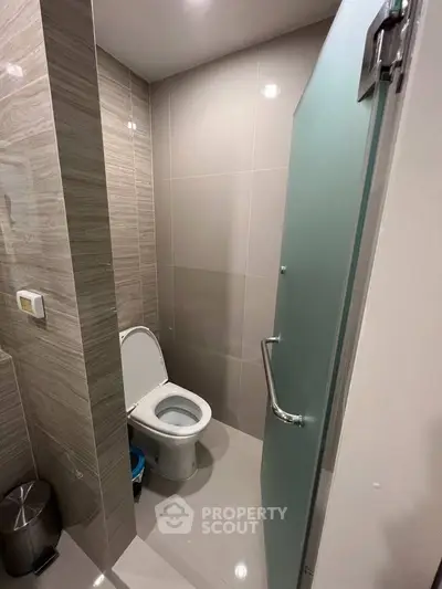 Modern bathroom with sleek design and frosted glass door, featuring a toilet and stylish wall tiles.