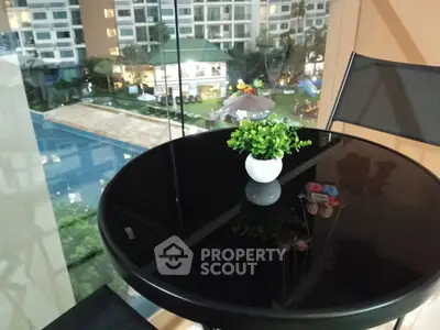 Modern balcony with glass railing overlooking pool and garden in luxury apartment complex.