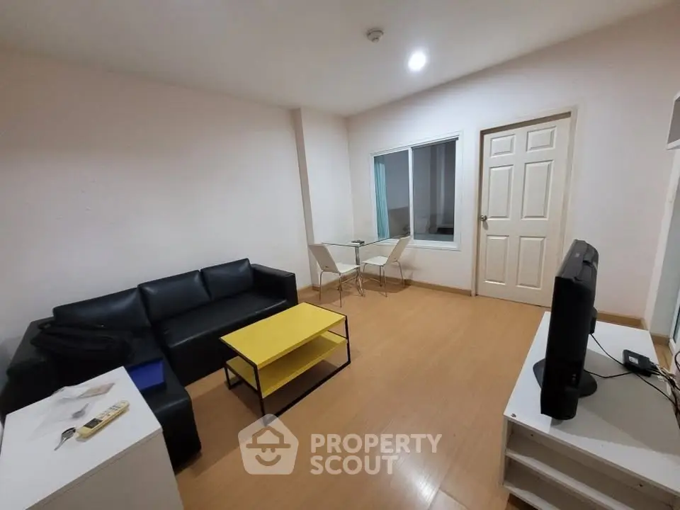 Modern living room with sleek black sofa, yellow coffee table, and flat-screen TV in a cozy apartment.