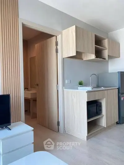 Modern compact kitchen with light wood cabinets and open shelving in a stylish apartment.
