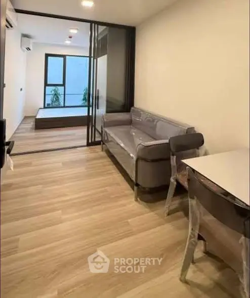 Modern living room with sleek furniture and wooden flooring, leading to a cozy bedroom.
