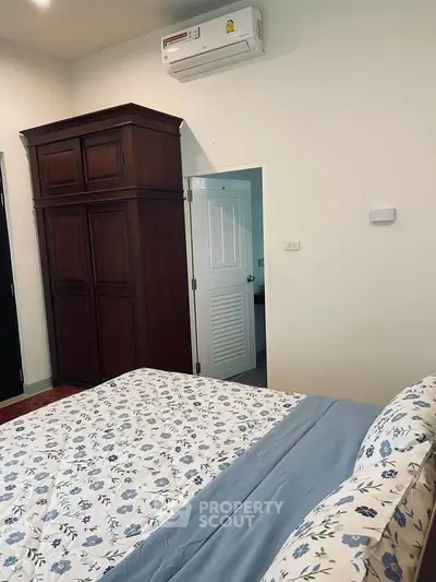 Cozy bedroom with floral bedding and wooden wardrobe, featuring air conditioning for comfort.