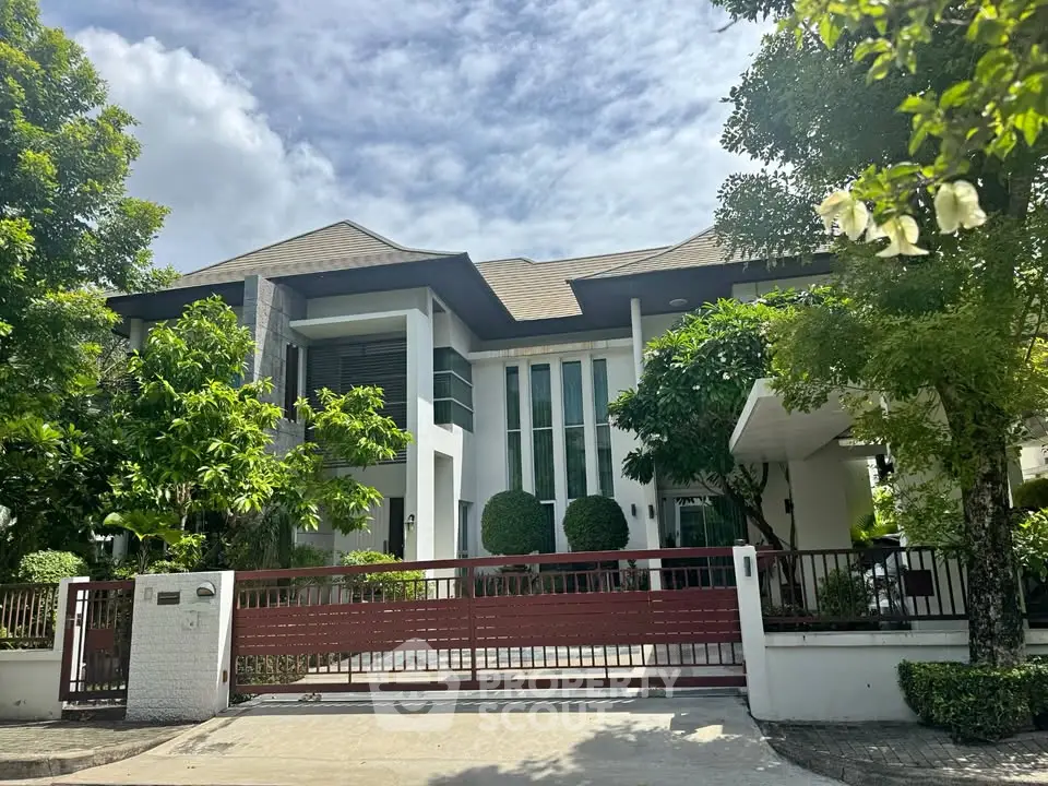 Luxurious modern house with lush greenery and spacious driveway in a serene neighborhood.