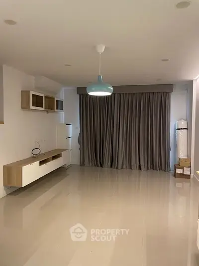 Spacious unfurnished living room with modern lighting and large window curtains.