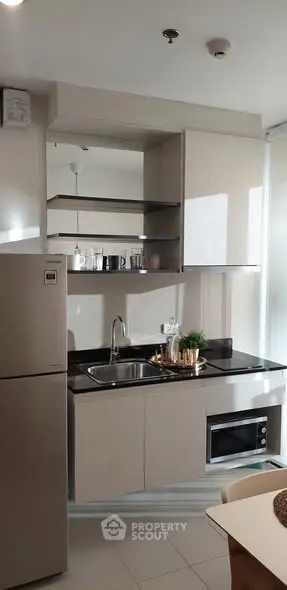 Modern kitchen with sleek cabinetry, built-in oven, and stainless steel fridge in a bright apartment.