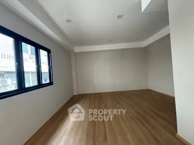 Spacious empty room with wooden flooring and large window, ideal for customization.