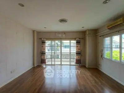Spacious empty living room with wooden flooring and large windows for natural light.
