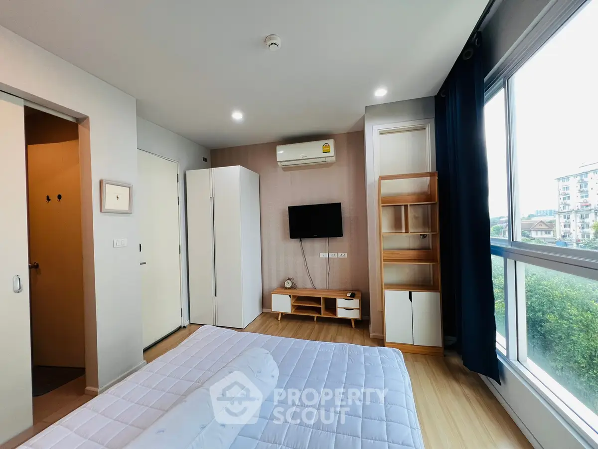 Modern bedroom with large window and stylish furniture in a high-rise apartment.