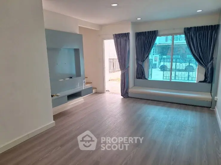 Spacious living room with large window and modern flooring, perfect for natural light lovers.