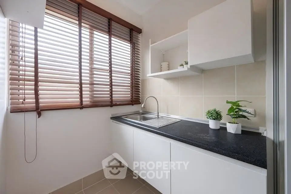 Modern kitchen with sleek countertops and natural light from large window blinds.