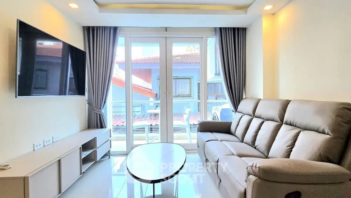 Modern living room with sleek sofa, wall-mounted TV, and large windows offering natural light.