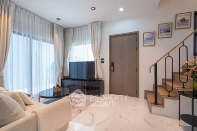 Modern living room with elegant decor and staircase, featuring a large TV and stylish furniture.