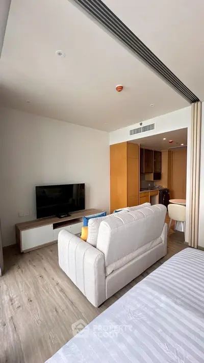 Modern living room with cozy sofa and sleek TV setup, open to a compact kitchen area.