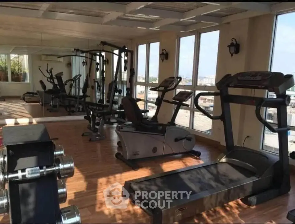 Spacious gym with modern equipment and large windows offering city views.