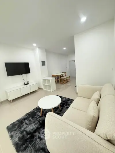Modern living room with sleek furniture and wall-mounted TV in a bright, minimalist apartment.