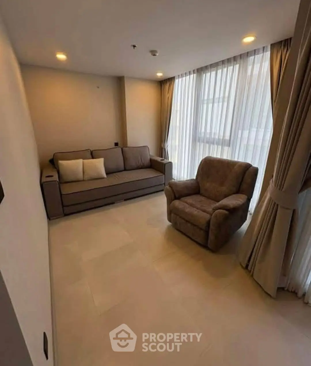 Cozy living room with modern sofa and armchair, large windows with elegant curtains.