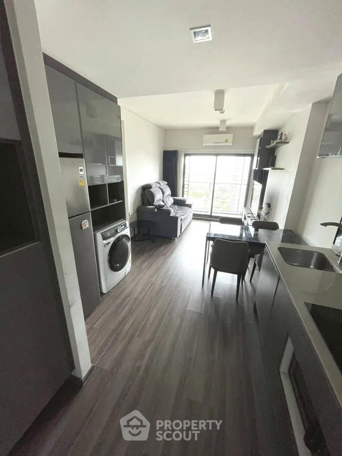 Modern apartment living room with sleek kitchen and washing machine, featuring large windows and stylish decor.