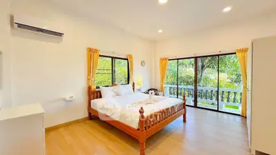 Spacious bedroom with large windows and garden view, featuring wooden flooring and modern furnishings.