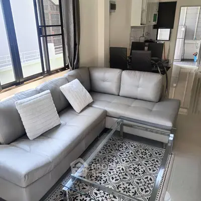 Modern living room with sleek gray sofa and glass coffee table, adjacent to a stylish kitchen.