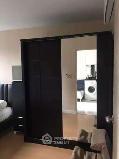 Modern bedroom with sliding wardrobe doors and view into laundry area with washing machine.