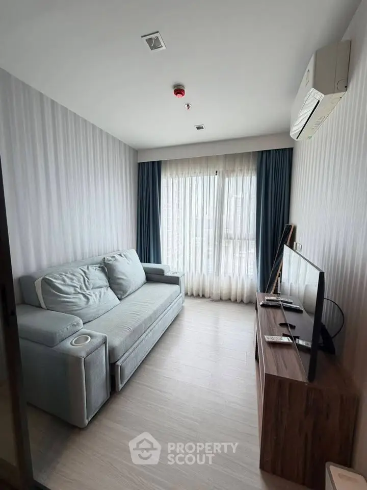 Modern living room with cozy sofa and flat-screen TV, featuring elegant curtains and air conditioning.