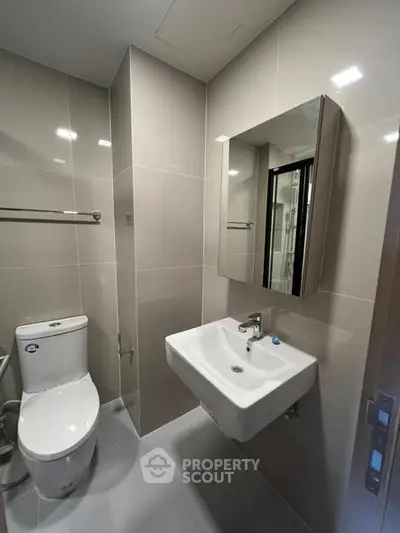 Modern bathroom with sleek fixtures and neutral tiles, featuring a wall-mounted sink and toilet.