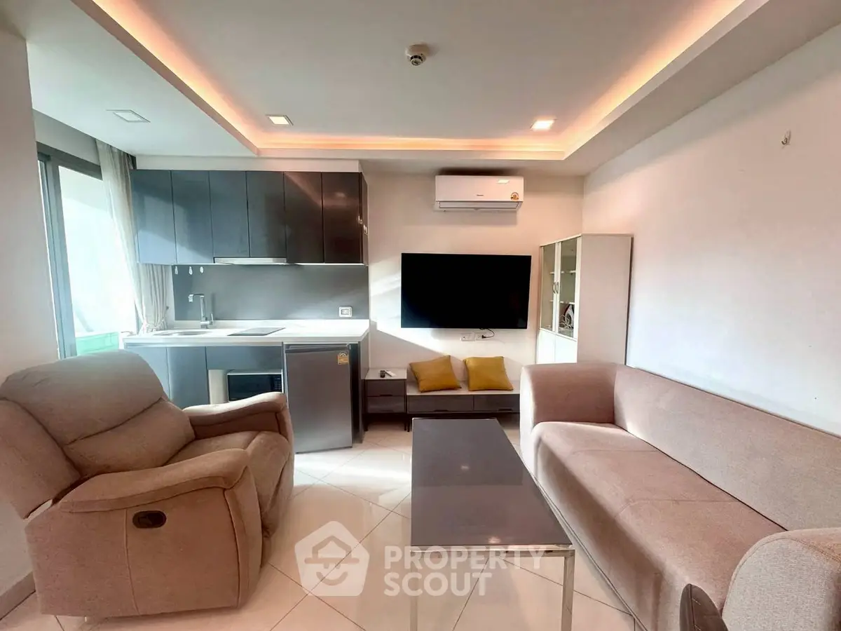 Modern living room with open kitchen, featuring sleek cabinetry and cozy seating area.
