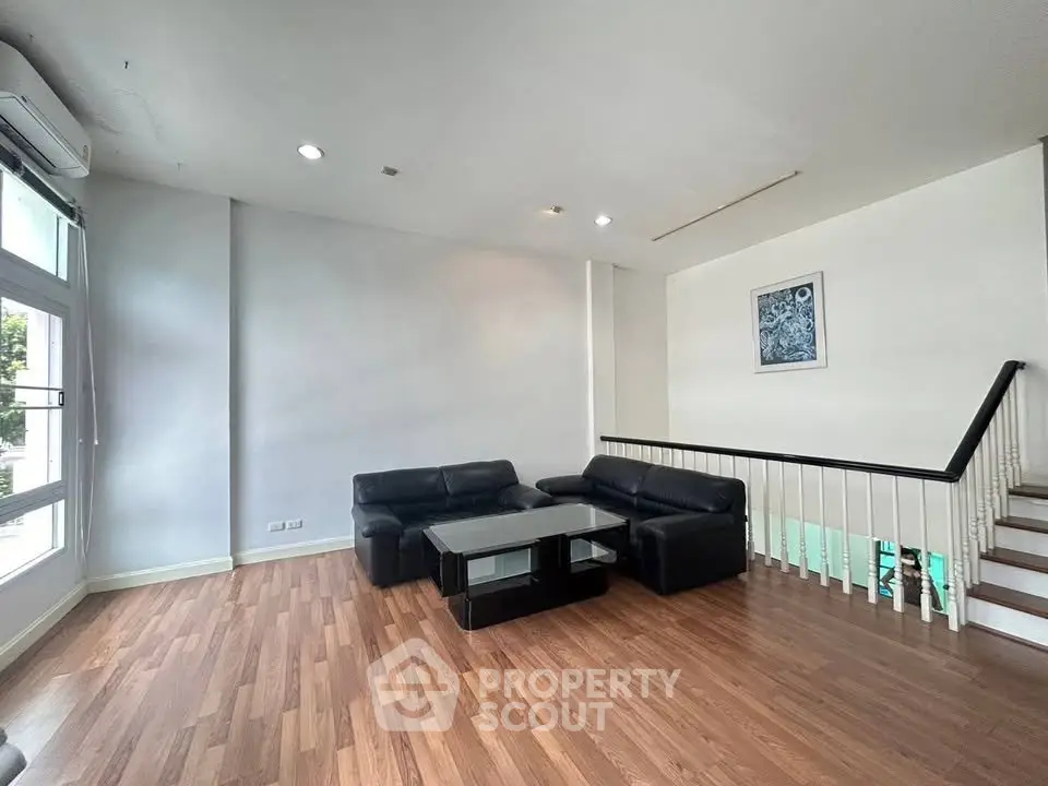 Spacious living room with modern black leather sofas and wooden flooring, perfect for relaxation and entertainment.