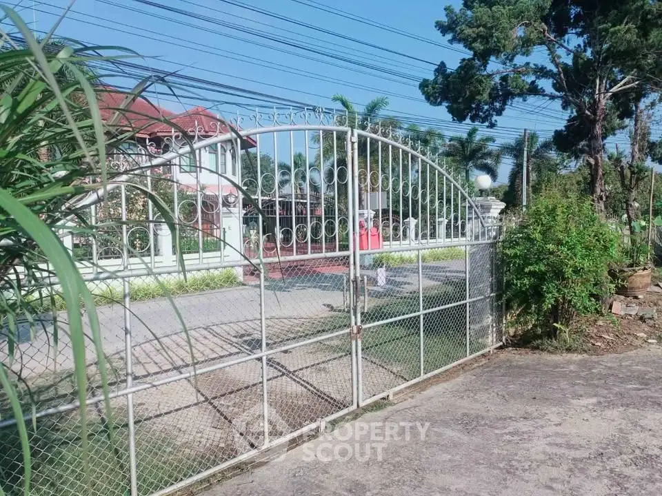 Charming gated entrance to a spacious property with lush greenery and a welcoming driveway.