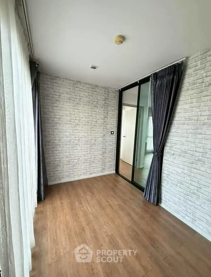 Spacious room with wood flooring and modern brick accent wall, perfect for versatile living space.