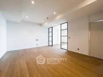 Spacious modern living room with wooden flooring and glass partition doors.