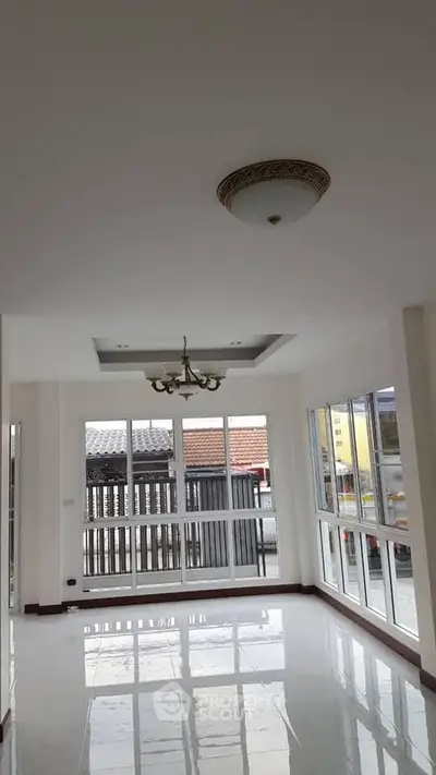 Spacious sunlit room with large windows and elegant ceiling light, perfect for modern living.