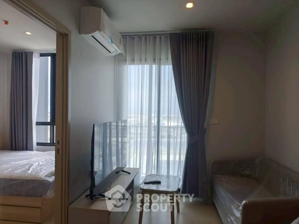 Modern apartment living room with TV, sofa, and large window with city view.
