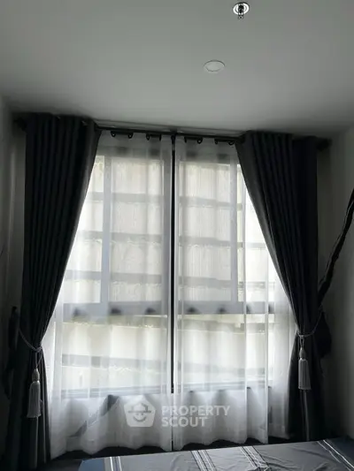 Cozy bedroom with large window and elegant curtains, offering natural light and a serene atmosphere.